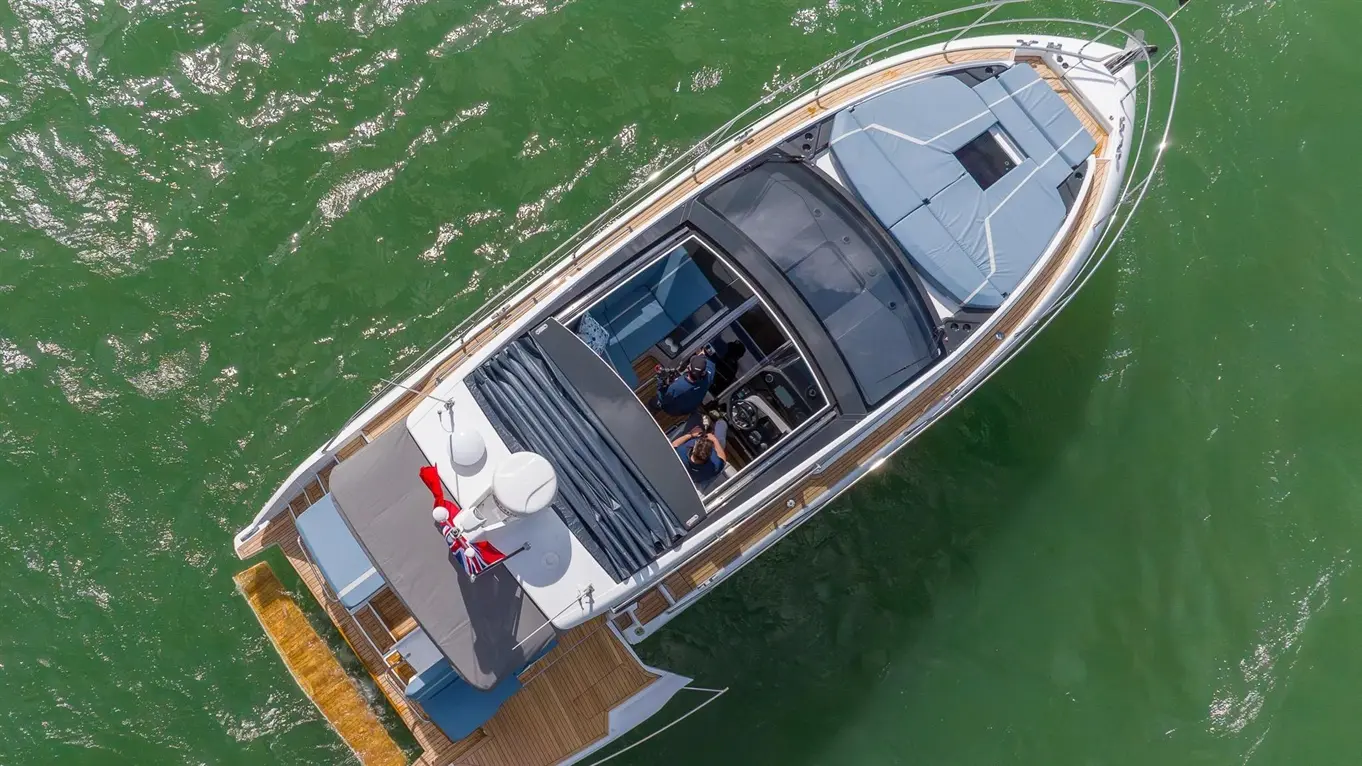 Aerial view of a modern motorboat on green water, featuring a grey sunshade and two people at the helm.